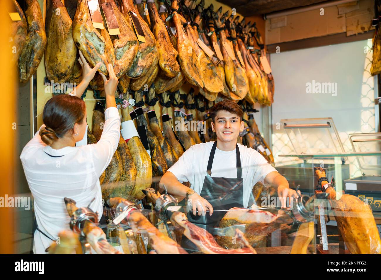 Junger Verkäufer in einer Schürze, der iberischen Jamon auf jamonera in der Metzgerei zerschneidet Stockfoto