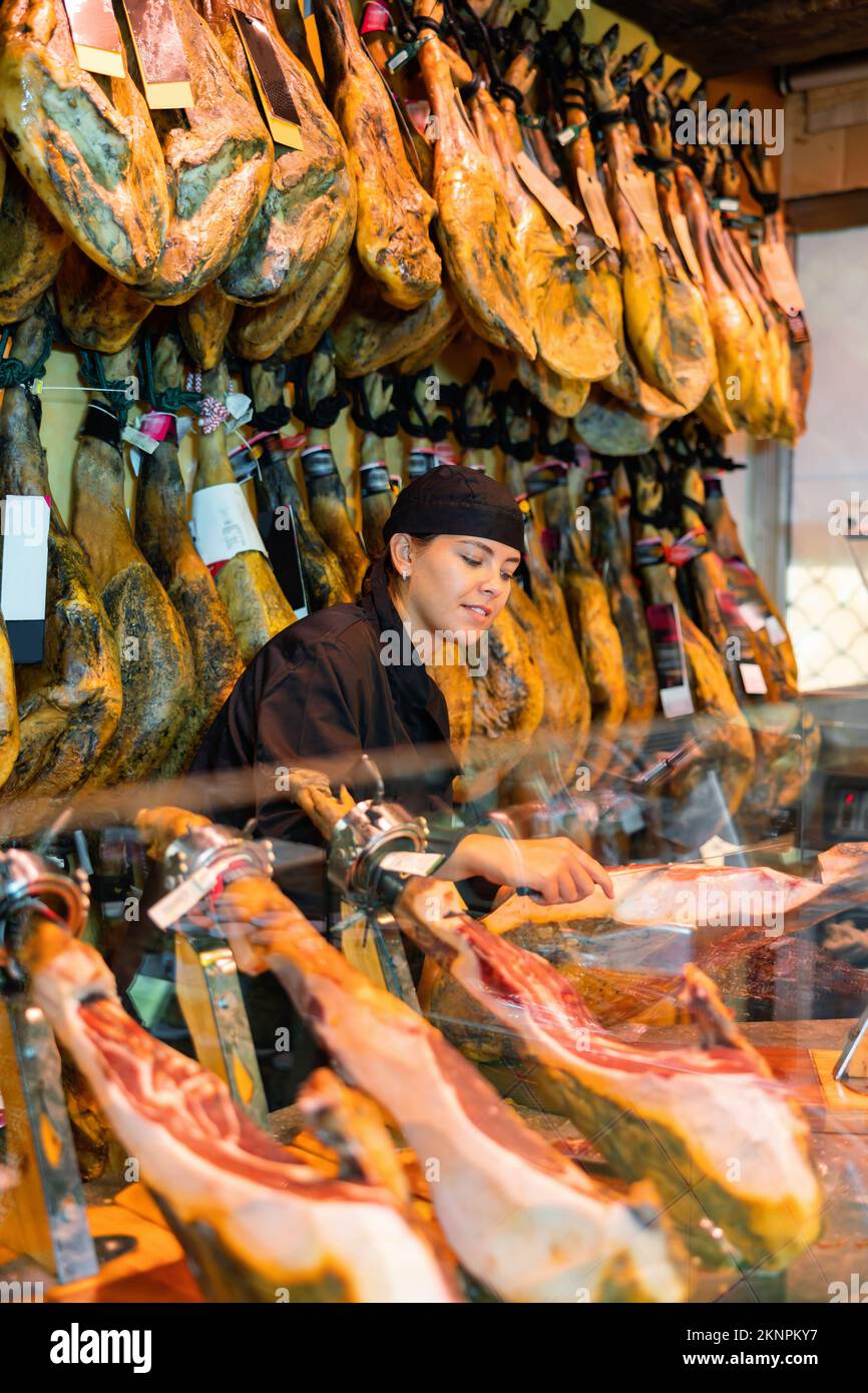 Weibliche Verkäuferin schneidet Scheiben aus dem ganzen Schenkel des Jamons im Fleischladen Stockfoto
