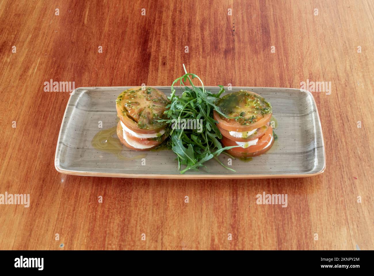 Eine Platte mit Käsesalat mit Tomatenstückchen mit Rucola und spanischem Olivenöl mit italienischer Pesto-Sauce Stockfoto