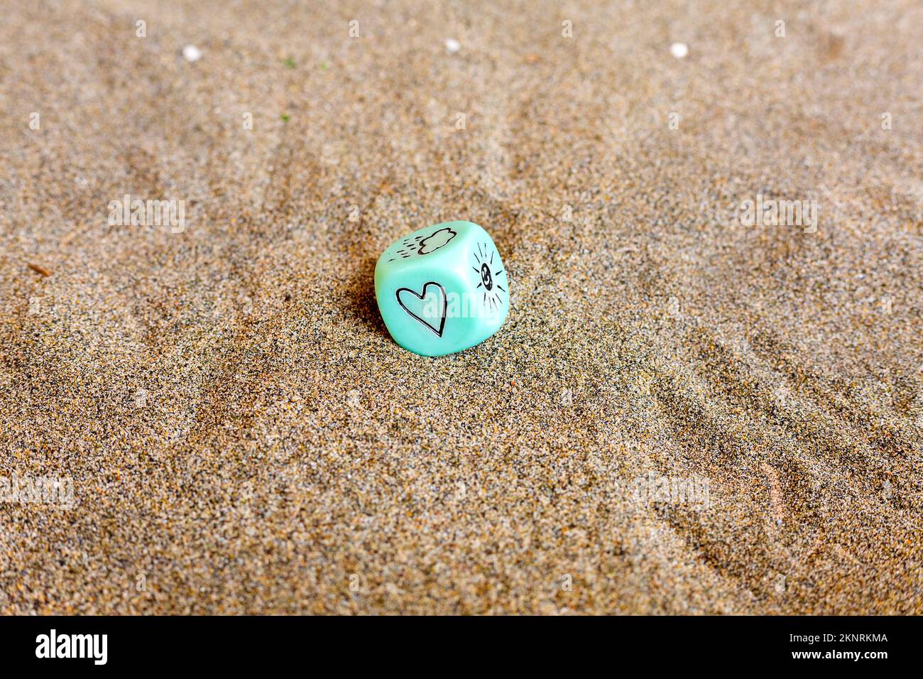 Wettervorhersage. Blauer Würfel mit Herz- und Wettersymbolen. Lustige Spielwürfel auf Sand. Valentinstag-Konzept. Liebessymbol. Nahaufnahme mit Stockfoto