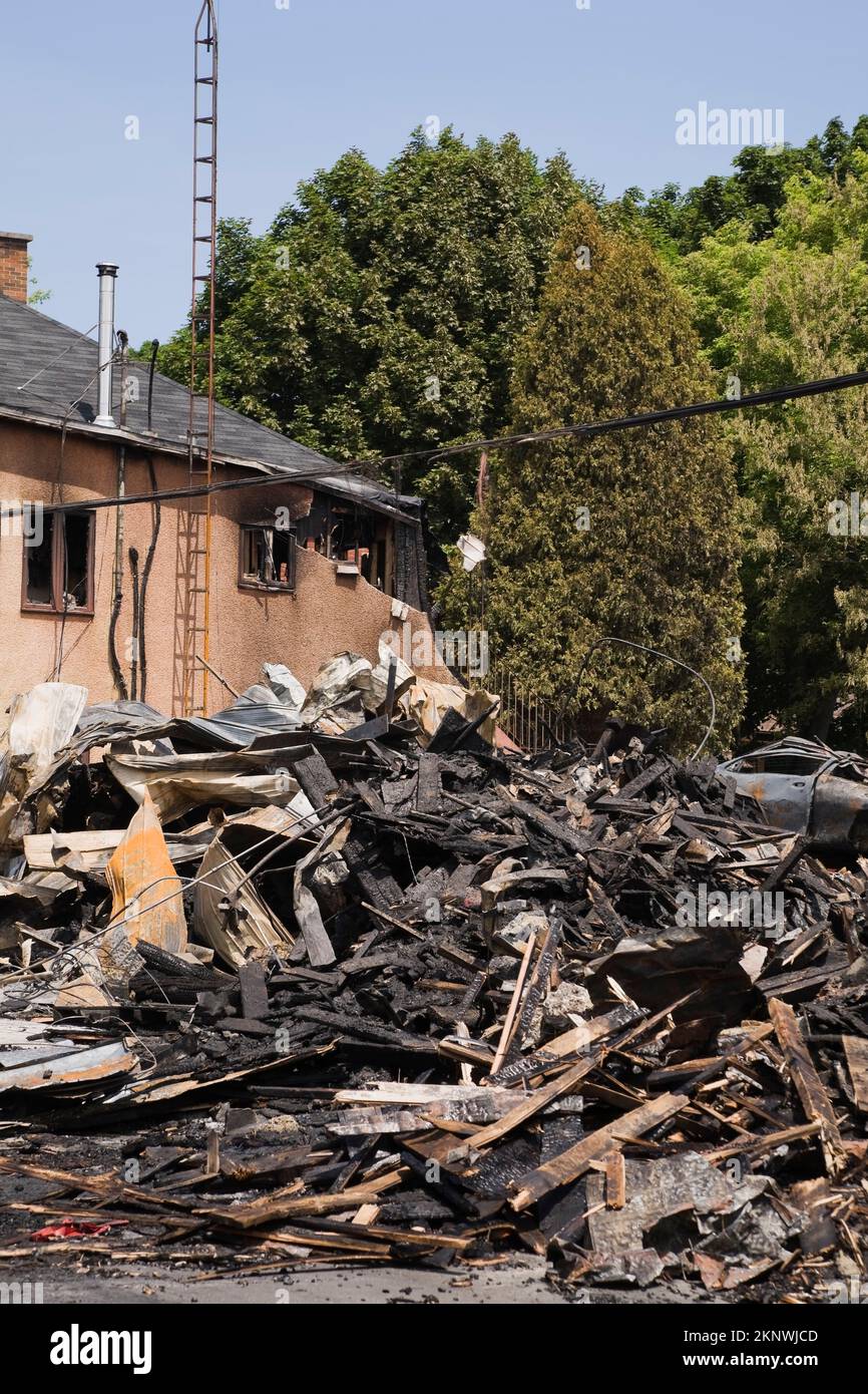 Durch Feuer beschädigtes Haus im Cottage-Stil neben Resten von abgebranntem Gewerbegebäude. Stockfoto