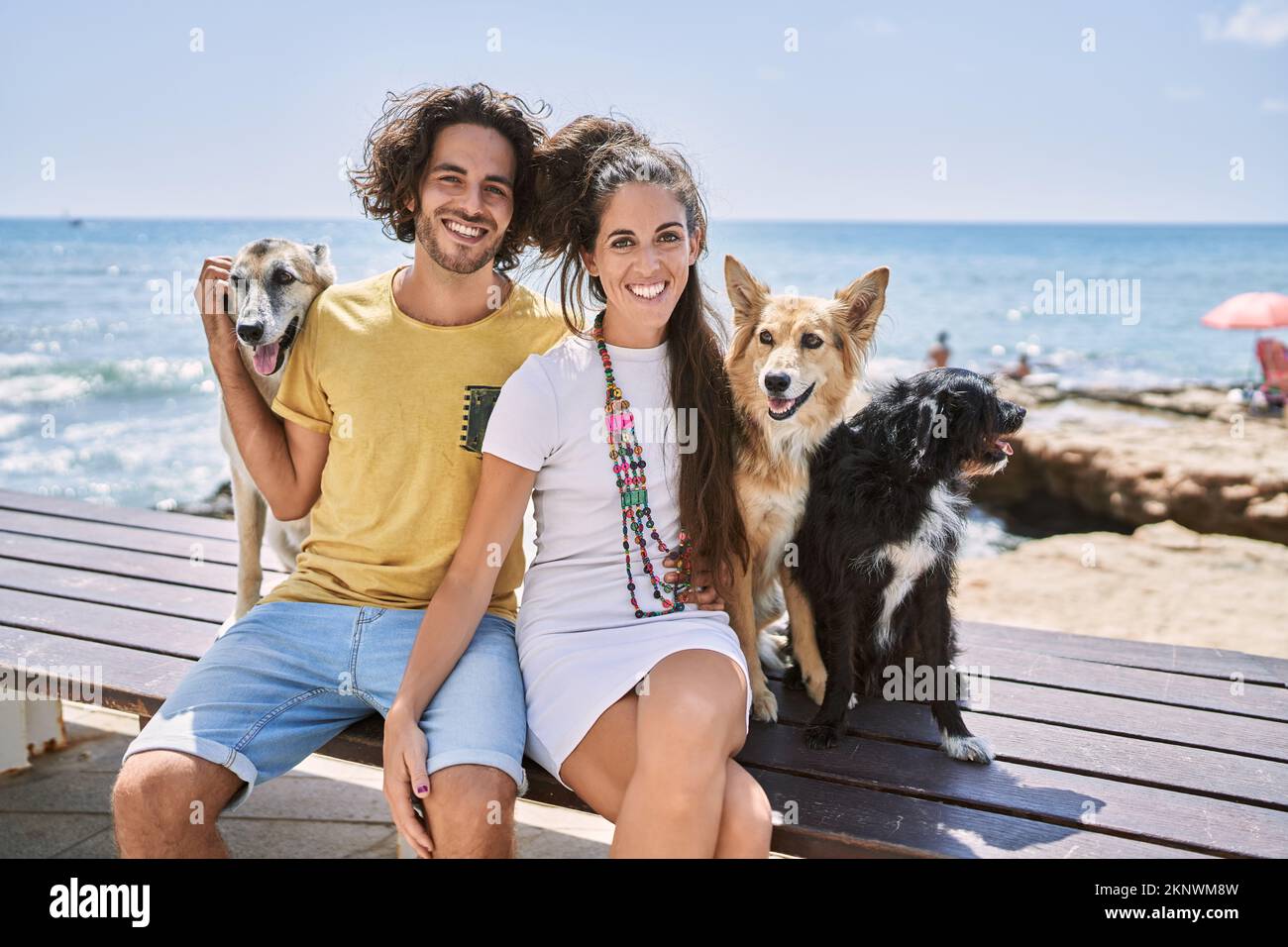 Mann und Frau Paar lächeln selbstbewusst und umarmen sich am Meer mit Hunden Stockfoto