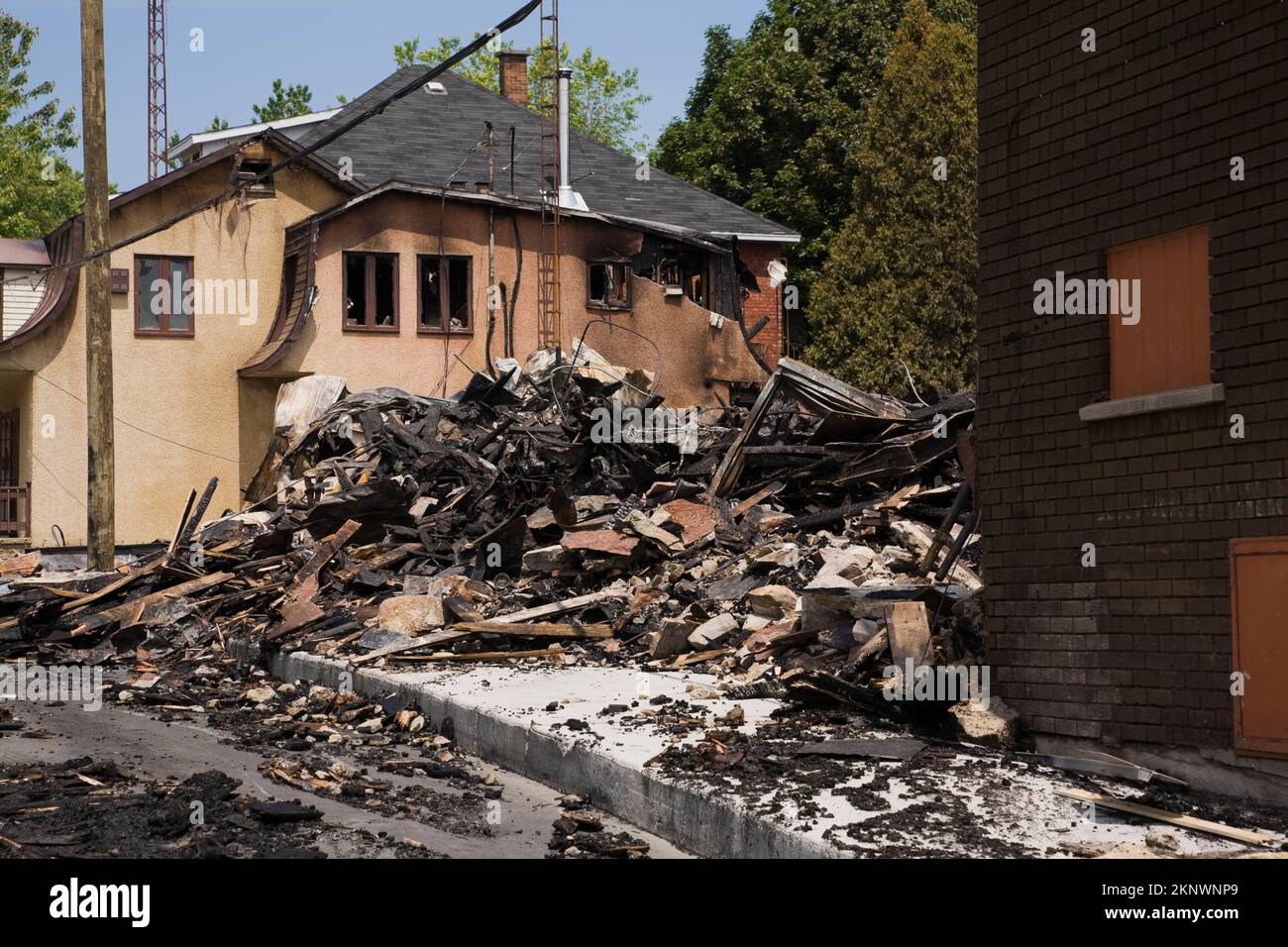 Durch Feuer beschädigtes Haus im Cottage-Stil neben Resten von abgebranntem Gewerbegebäude. Stockfoto