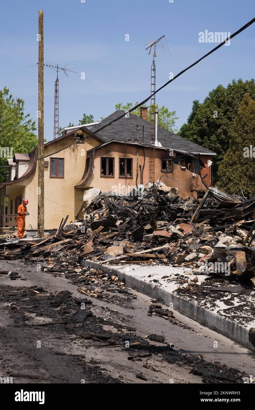 Reinigungskräfte neben einem Feuer beschädigten Haus im Cottage-Stil mit Resten eines abgebrannten Gewerbegebäudes. Stockfoto