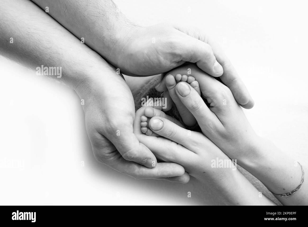 Beine, Zehen, Füße und Fersen eines Neugeborenen. Mit den Händen der Eltern, Vater, Mutter hält sanft die Beine des Kindes. Stockfoto