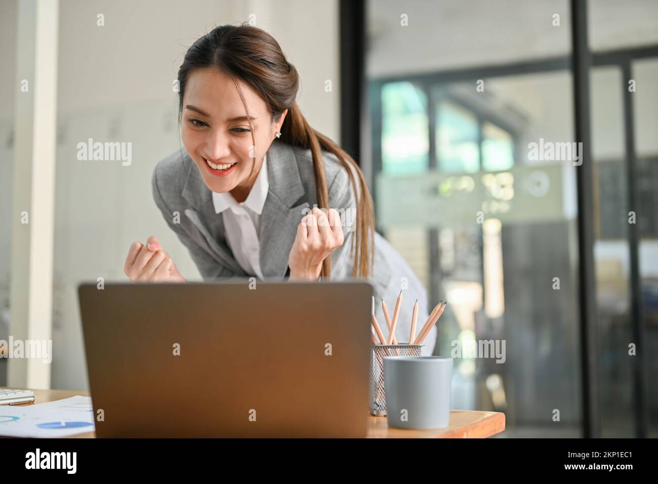 Glückliche asiatische Geschäftsfrau, die ihren Erfolg feiert, lächelt, auf den Laptop-Bildschirm schaut und eine E-Mail zur Stellenbeförderung erhält. Stockfoto