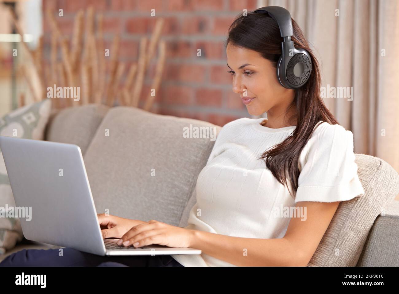 Streamen von Musikvideos. Eine attraktive junge Frau, die Kopfhörer trägt, während sie ihr Notebook zu Hause benutzt. Stockfoto