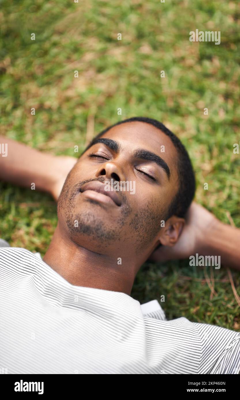Zeit für ein Nickerchen im Freien. Ein gutaussehender junger Mann, der draußen auf dem Gras liegt. Stockfoto