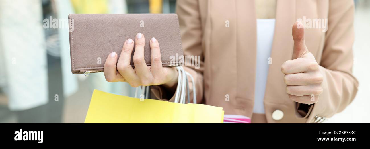 Frau hält die Brieftasche voll mit Bargeld, zeigt Daumen nach oben Geste mit dem Finger Stockfoto