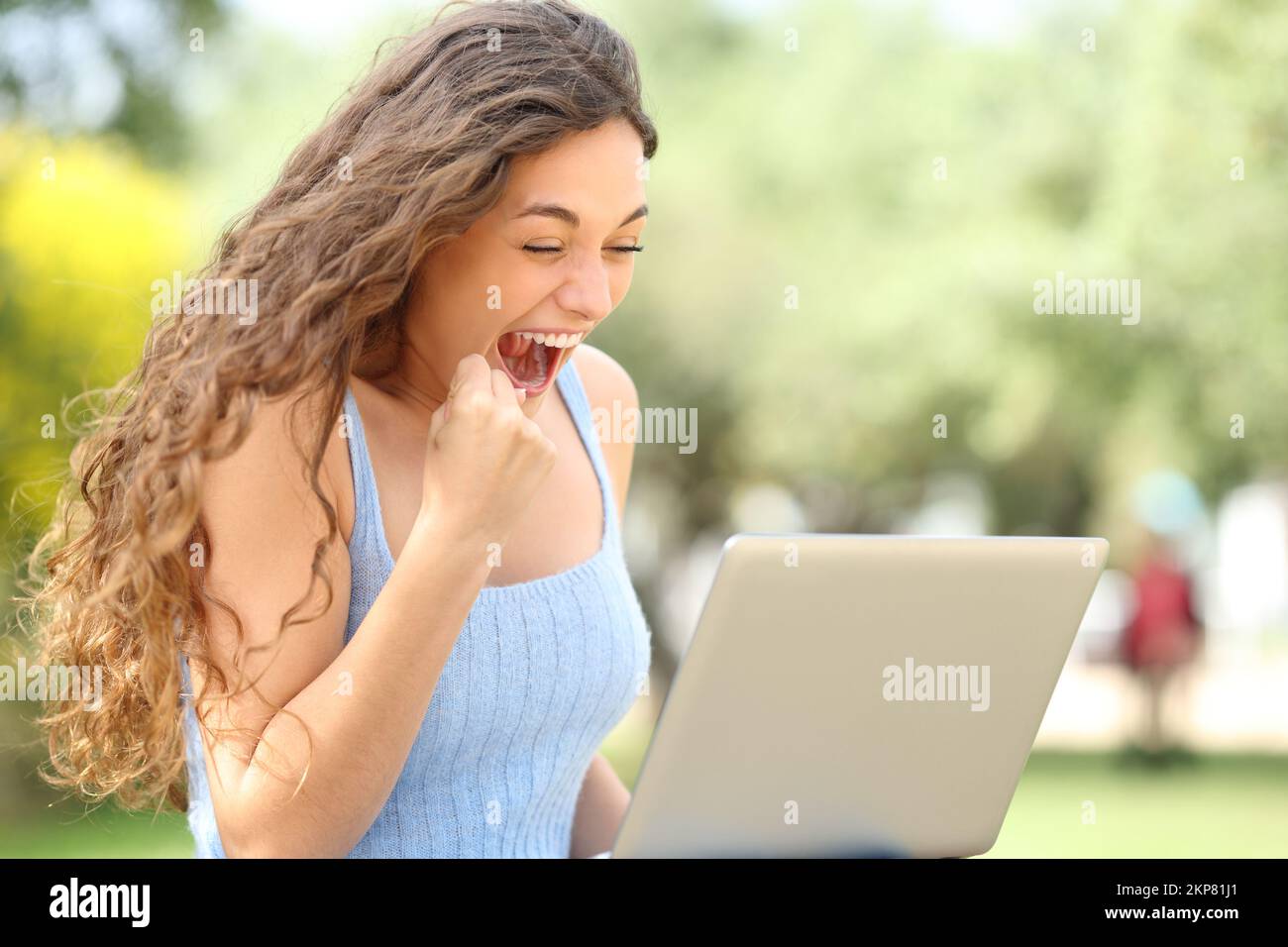 Aufgeregte Frau feiert Erfolg mit einem Notebook im Park Stockfoto