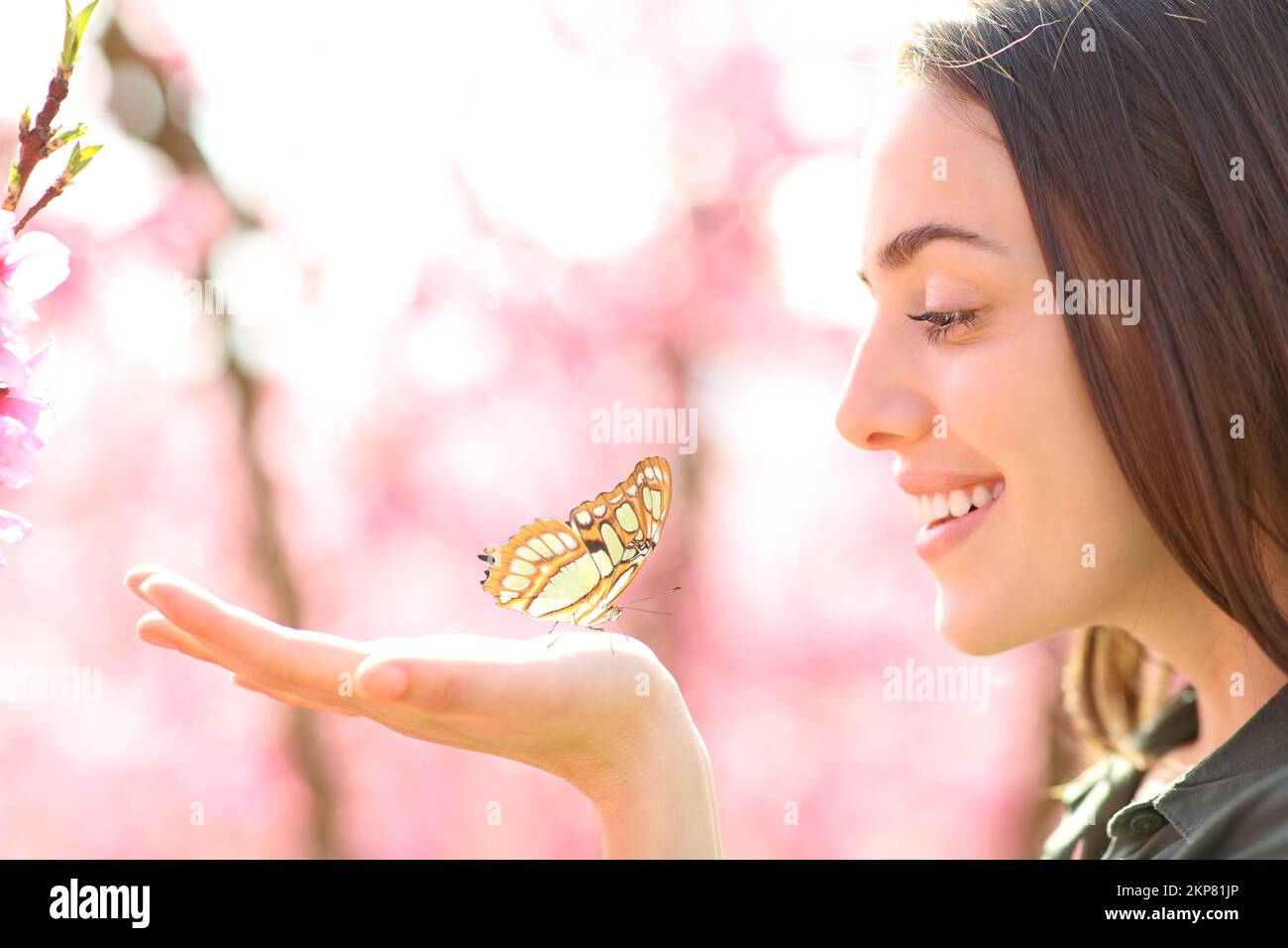 Eine glückliche Frau mit einem Schmetterling in der Hand, die ihn ansieht Stockfoto