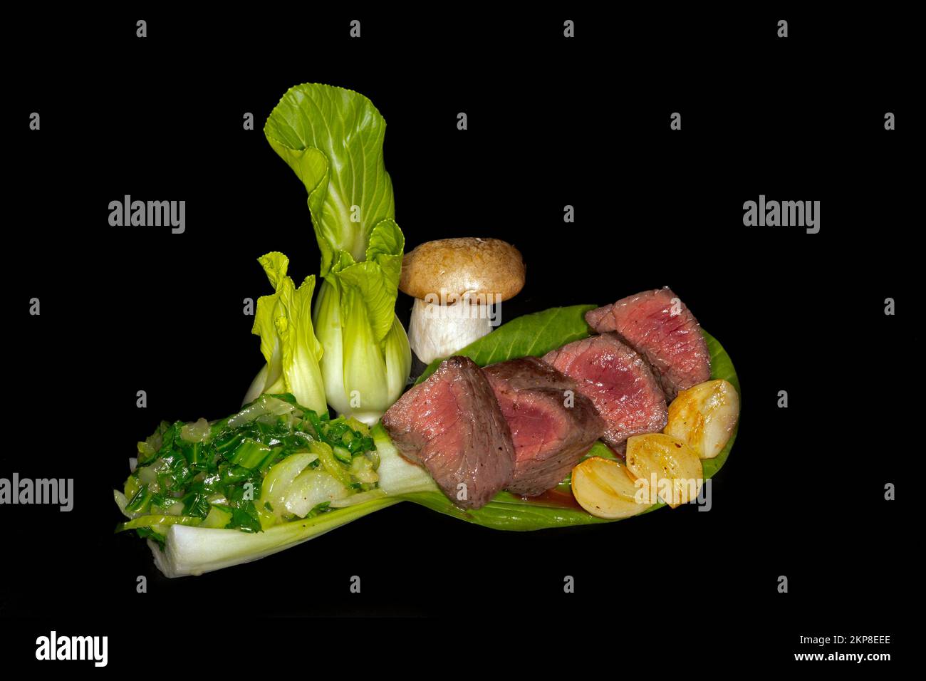 Mittelgeröstetes Wildfilet mit pak Choi, Kräuterpilzen und Knoblauch, Lebensmittelfotografie mit schwarzem Hintergrund Stockfoto