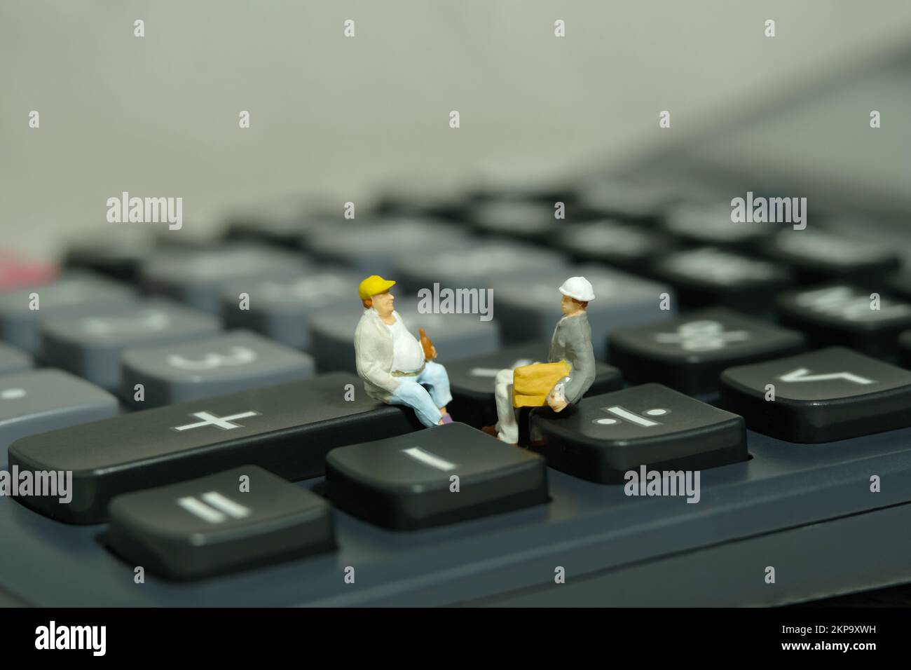 Miniatur-Menschen-Spielzeug-Figuren-Fotografie. Besprechung des Projektbudgets. Zwei Arbeiter, die über dem Taschenrechner sitzen. Bildfoto Stockfoto