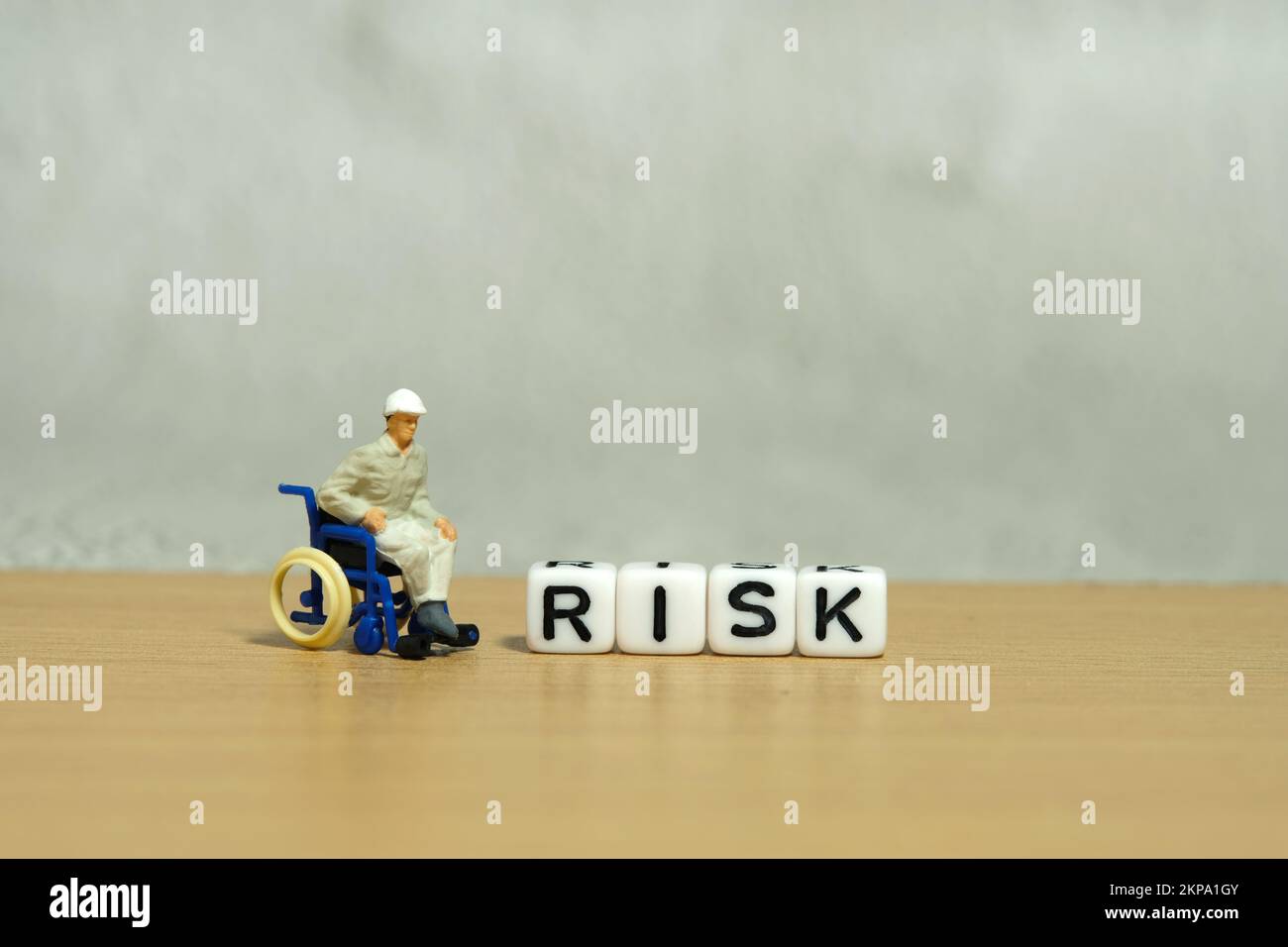 Miniatur-Menschen-Spielzeug-Figuren-Fotografie. Konzept der Arbeitssicherheitsgarantie. Männer Arbeiter, die auf Rollstuhl neben DEM RISIKOWÜRFEL sitzen. Bildfoto Stockfoto