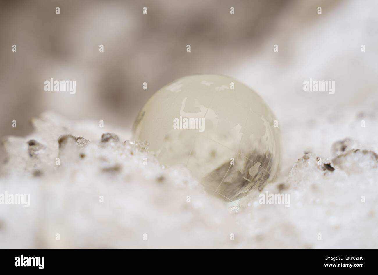 Die Glaskugel liegt auf einem schmutzigen Schneeverwehung oder vereisten Hintergrund mit Sonnenstrahlen. Stockfoto