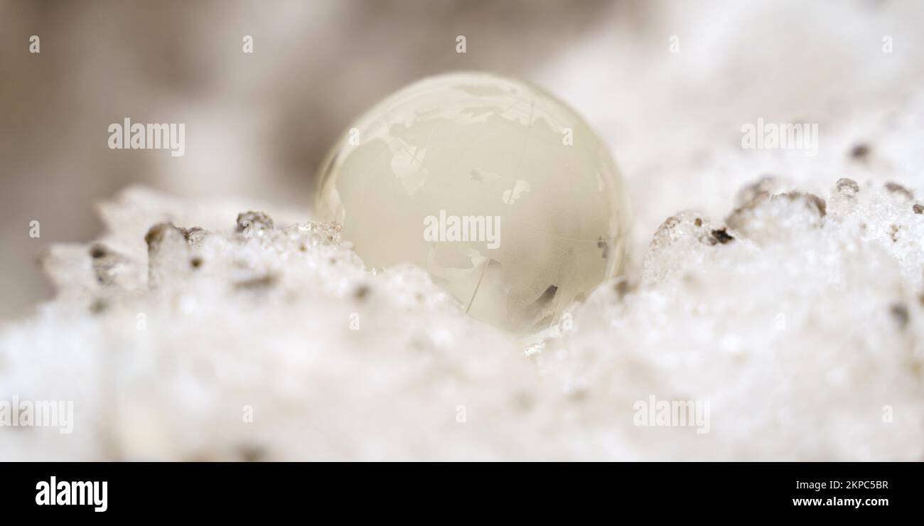 Die Glaskugel liegt auf einem schmutzigen Schneeverwehung oder vereisten Hintergrund mit Sonnenstrahlen. Stockfoto
