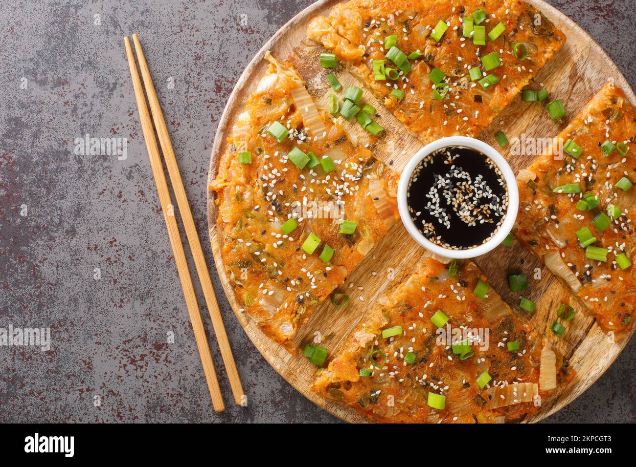 Kimchijeon ist ein koreanischer pikanter, knuspriger Pfannkuchen aus Kimchi mit Mehl und Zwiebeln auf dem Holzbrett auf dem Tisch. Horizontale Draufsicht von ab Stockfoto
