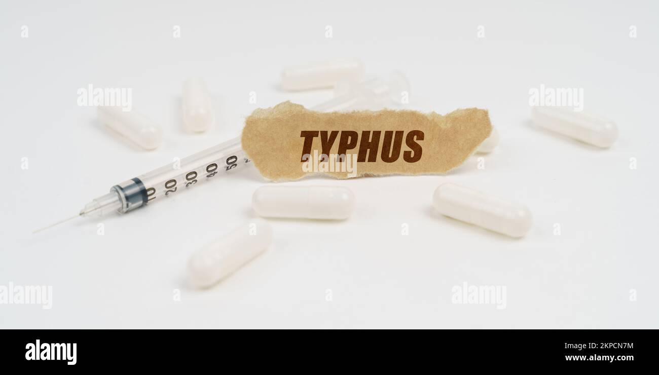 Medizin und Gesundheitskonzept. Auf einem weißen Tisch sind Pillen, eine Spritze und ein Stück Papier mit der Inschrift - TYPHUS Stockfoto