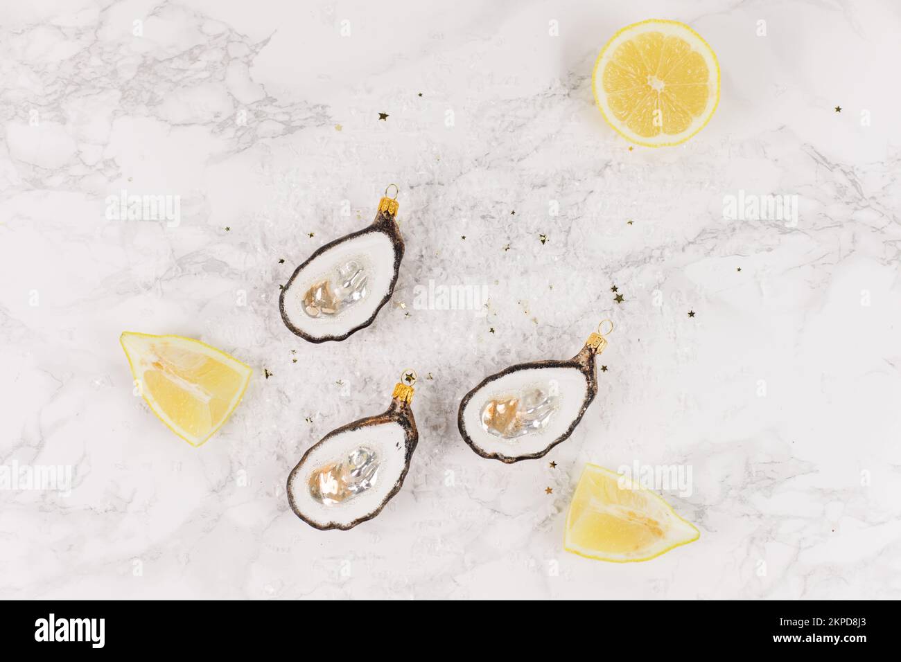 Drei Weihnachtsbaumkugeln in Form einer Auster liegen auf einem Marmortisch. Glitzer, Sterne und Zitronenscheiben schmücken das Bild. Stockfoto