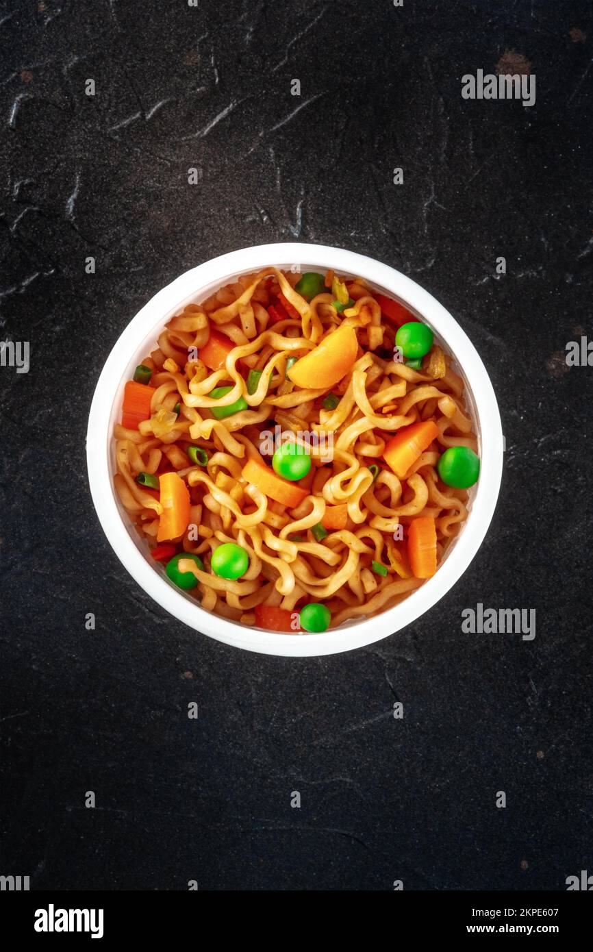 Ramen-Tasse, Instant-Soba-Nudeln in einem Plastikbecher mit Gemüse, von oben auf schwarzem Hintergrund mit einem Platz für Text aufgenommen Stockfoto