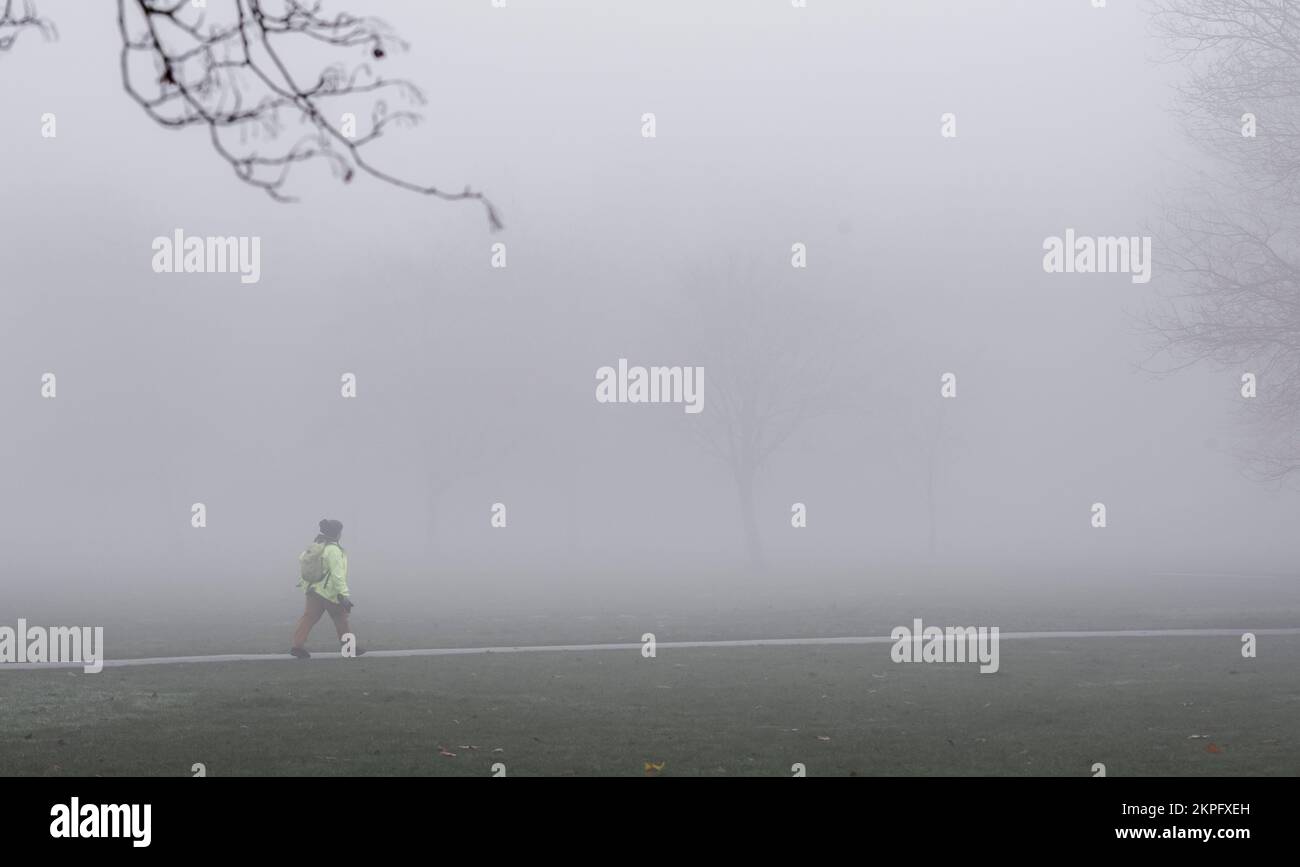 Harrogate, Großbritannien. 28.. November 2022. Eine unheimliche Landschaft wurde heute Morgen durch den Nebel auf der Stray im Stadtzentrum geschaffen. Eine Dame mit Warnweste geht durch den Park. Bildnachweis: ernesto rogata/Alamy Live News Stockfoto