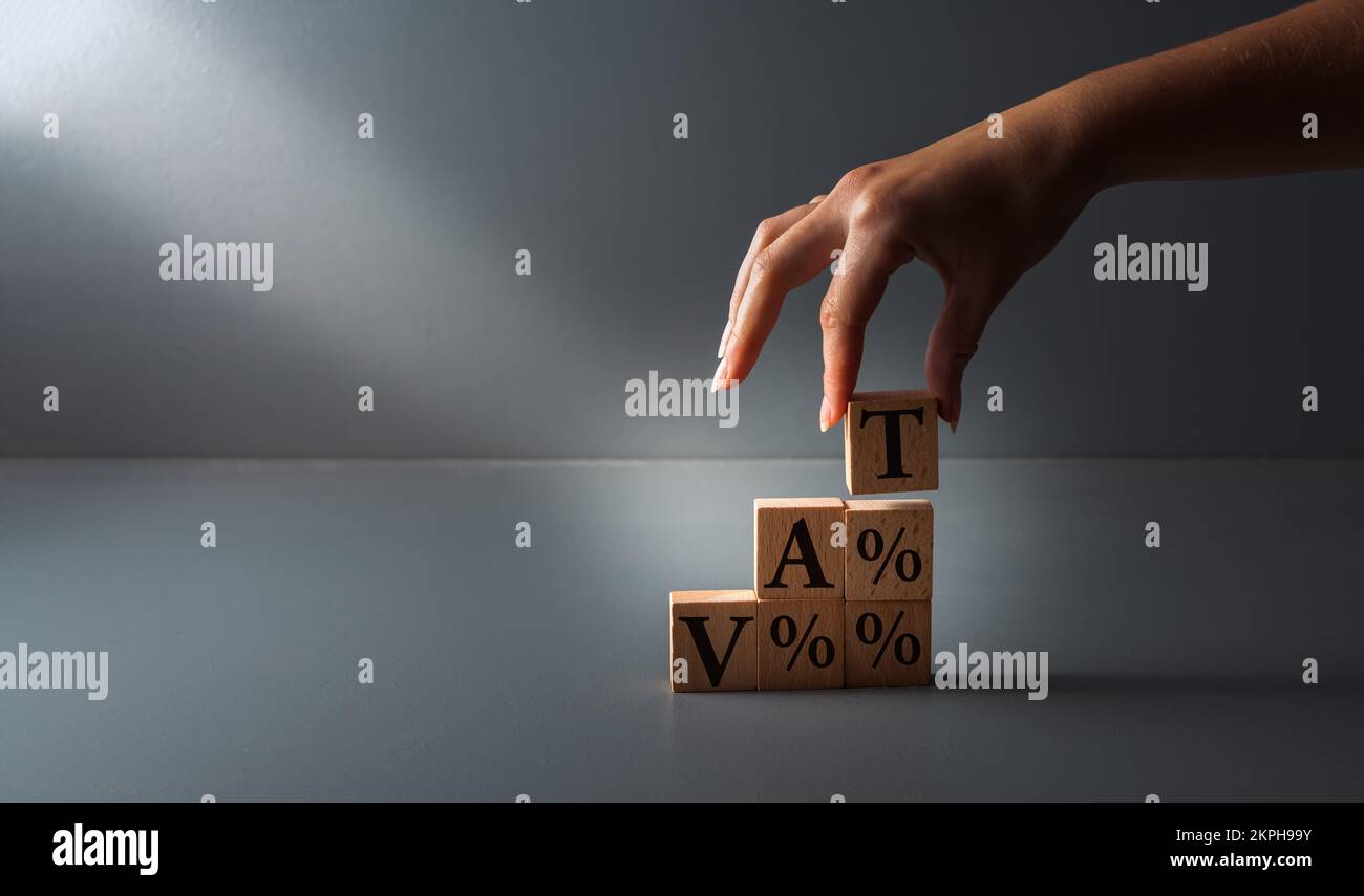 Holzklötze mit der Hand mit Fass oder Mehrwertsteuer. Konzept der Steuerzahlung , auf grauem Hintergrund . Stockfoto
