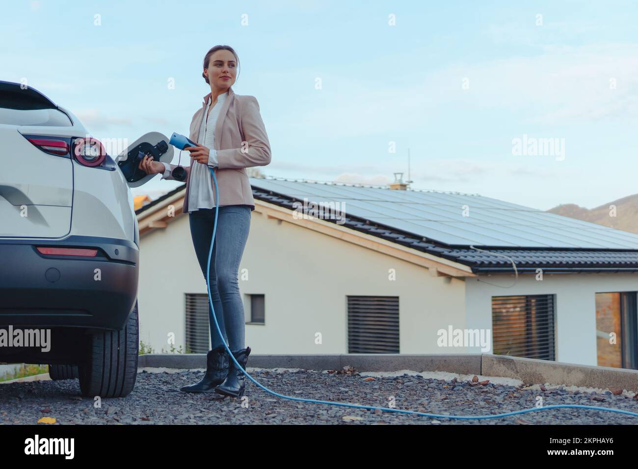 Junge Frau lädt ihr Elektroauto im nachhaltigen und wirtschaftlichen Transportkonzept zu Hause. Stockfoto