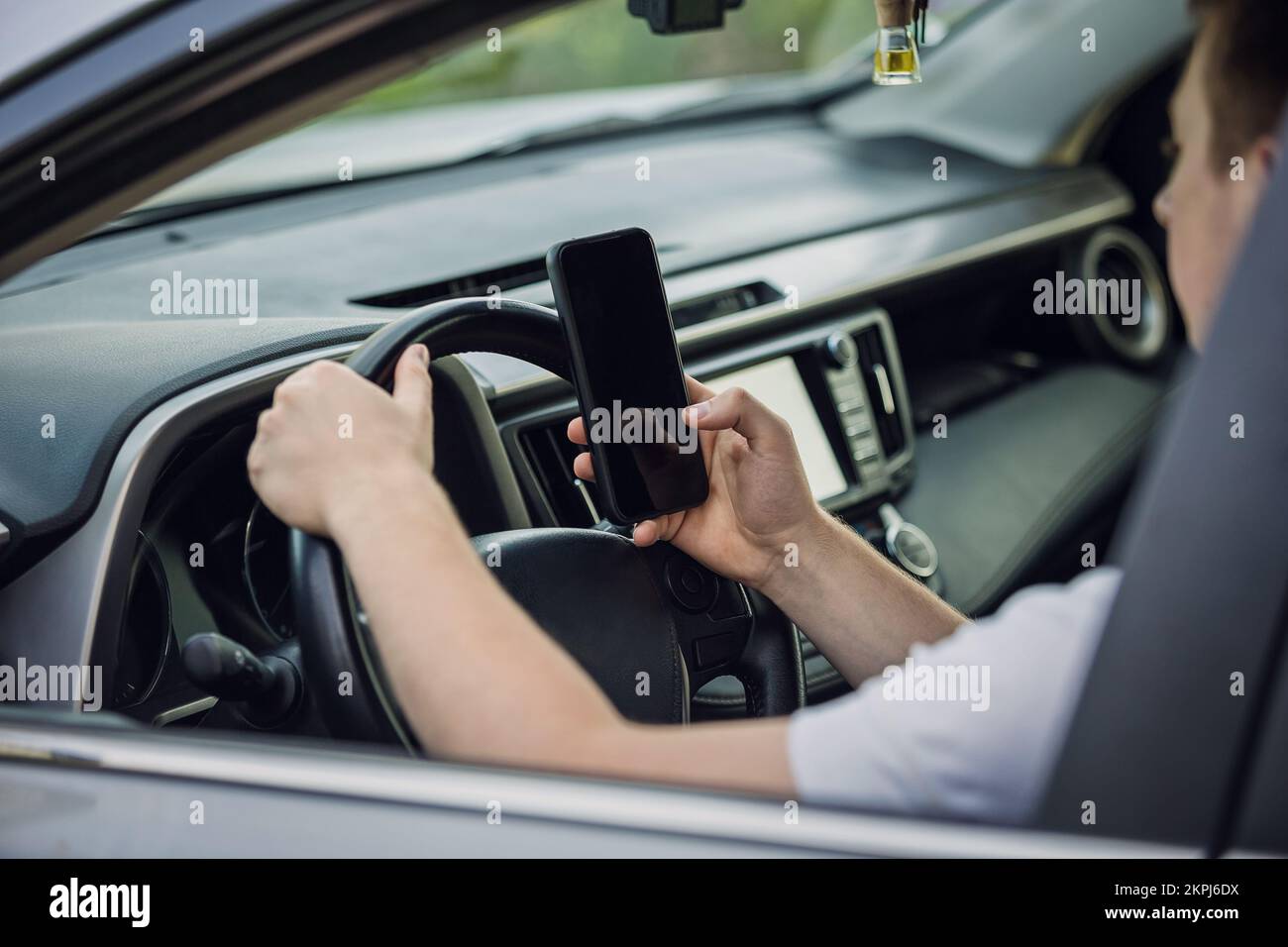 Ein Gelegenheitsfahrer, der vor dem Lenkrad von seinem Telefon abgelenkt wurde und sein Smartphone während der Fahrt mit einer Hand benutzte. Risiko- und Gefahrenlage Stockfoto