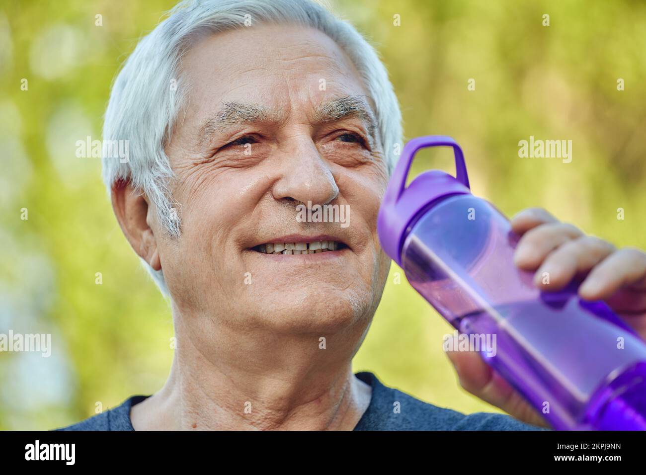 Nahaufnahme attraktiver reifer Mann hält wiederverwendbare Plastikflasche, die stilles Mineralwasser trinkt, während des Morgentrainings oder Spaziergangs im Sommerpark carin Stockfoto