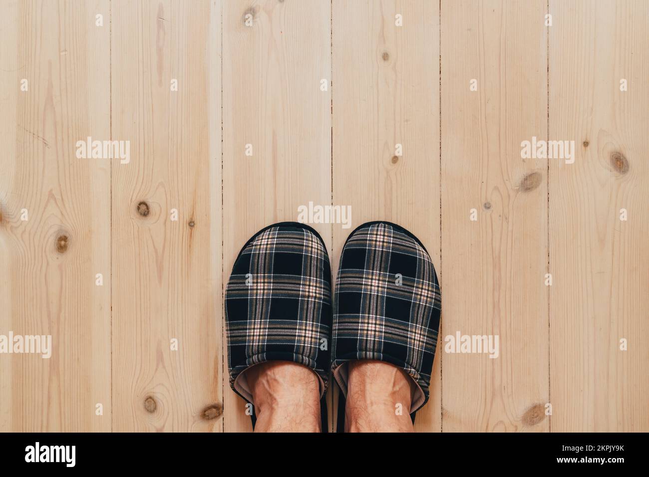 Draufsicht auf männliche Füße, die Heimschuhe tragen und auf dem Hartholzboden im Wohnzimmer stehen, Kopierbereich inbegriffen Stockfoto