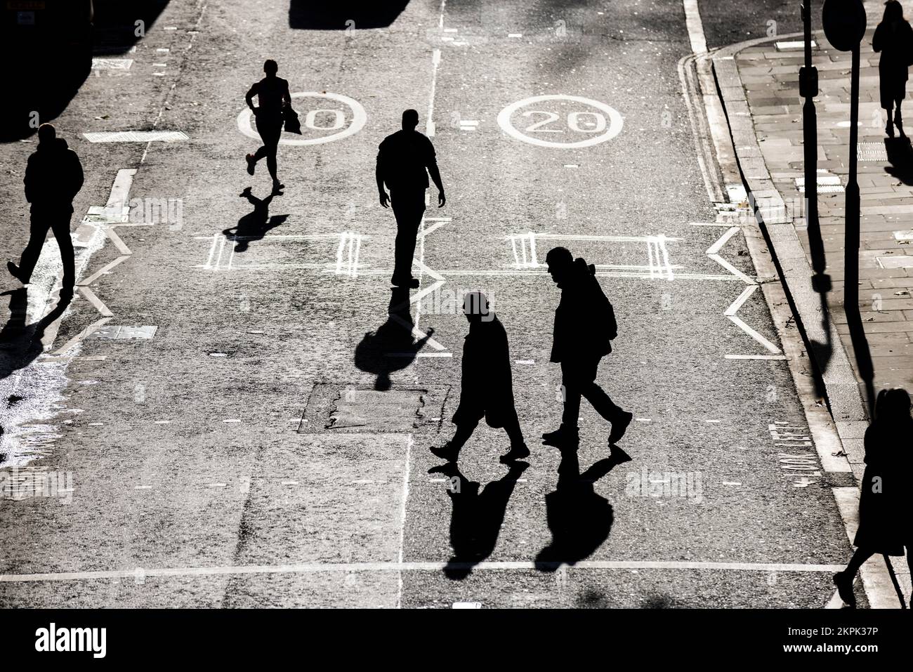 An einem sonnigen Wintertag in der City of London, England, Großbritannien, gehen die Silhouetten der Arbeiter über eine Fußgängerüberquerung Stockfoto