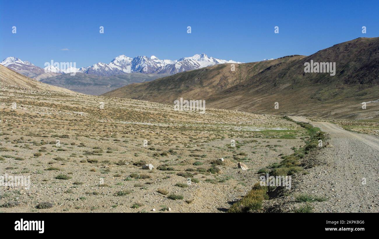 Malerischer Landschaftsblick mit unbefestigter Straße und schneebedeckten Bergen im hoch gelegenen Khargush Pass, Gorno-Badakshan, Tadschikistan Pamir Stockfoto