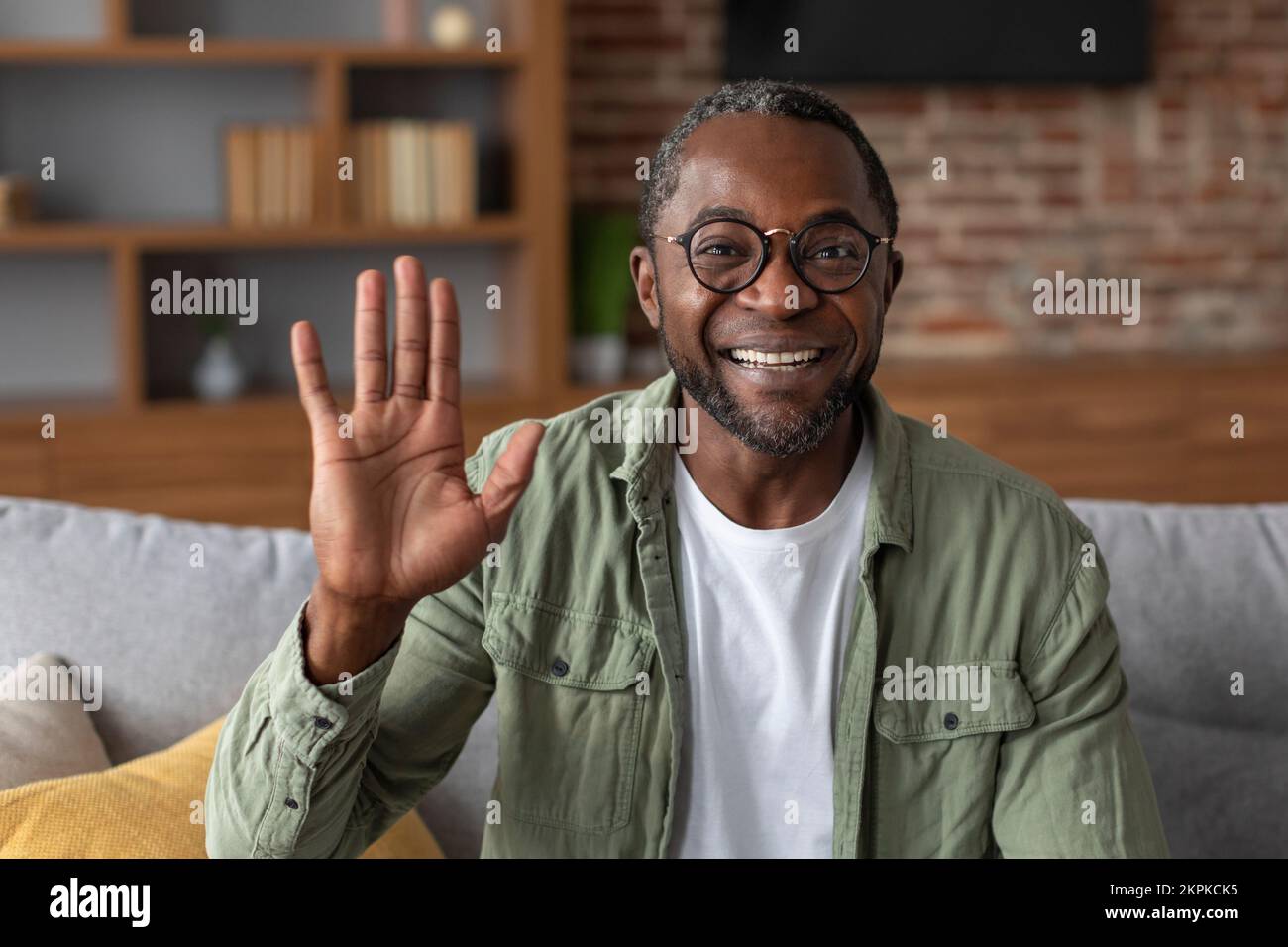 Porträtfoto eines lächelnden afroamerikanischen Mannes mittleren Alters, der Hand vor der Kamera winkt, grüßt, sagt Hallo, hat Videoanruf Stockfoto