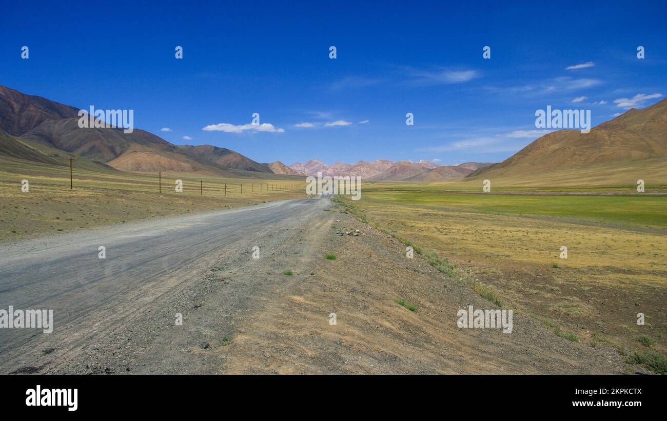 Malerische Berglandschaft auf einem langen, geraden Straßenabschnitt auf dem hoch gelegenen Pamir Highway nahe Murghab, Gorno-Badakshan, Tadschikistan Stockfoto