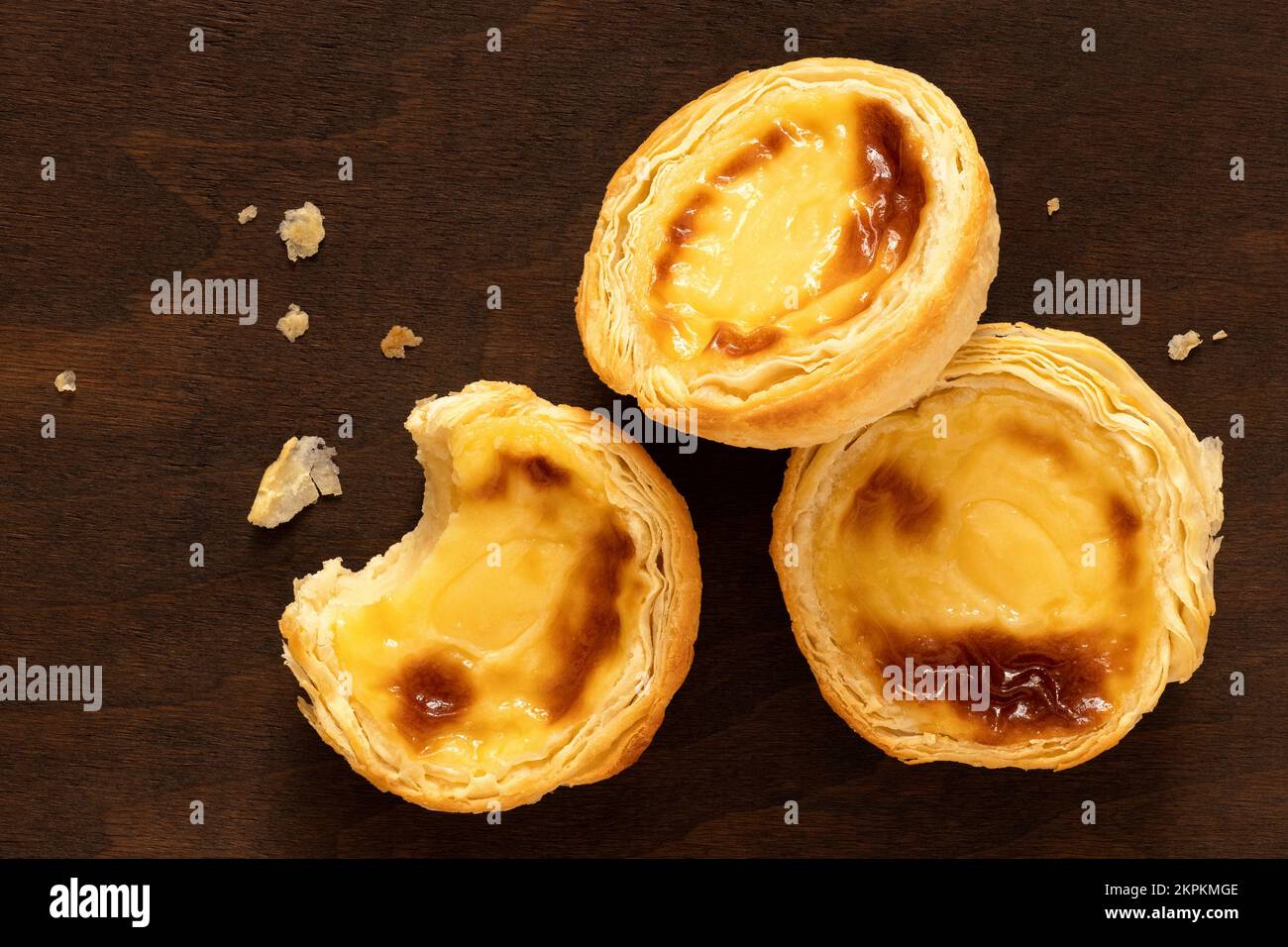 Drei portugiesische Puddingeiertorten mit Krümeln auf dunklem Holzhintergrund. Draufsicht. Stockfoto