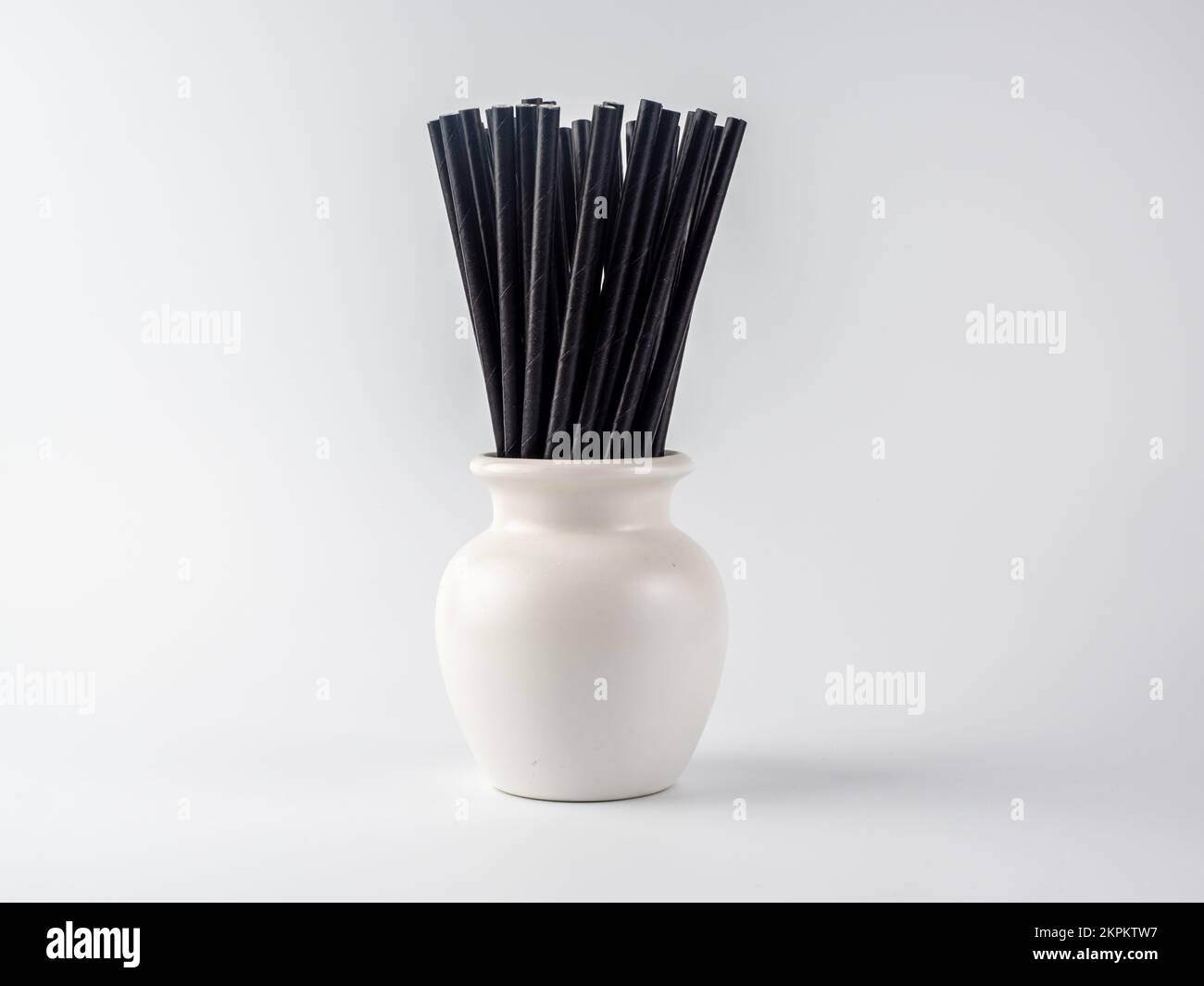 Weißer Vase-Topf mit schwarzen, biologisch abbaubaren Bambus-Cocktailstäbchen auf weißem Hintergrund Stockfoto