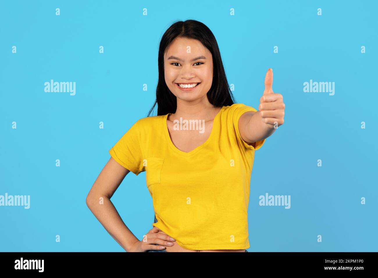 Eine zufriedene japanische Studentin im gelben T-Shirt zeigt Daumen hoch und schaut in die Kamera Stockfoto