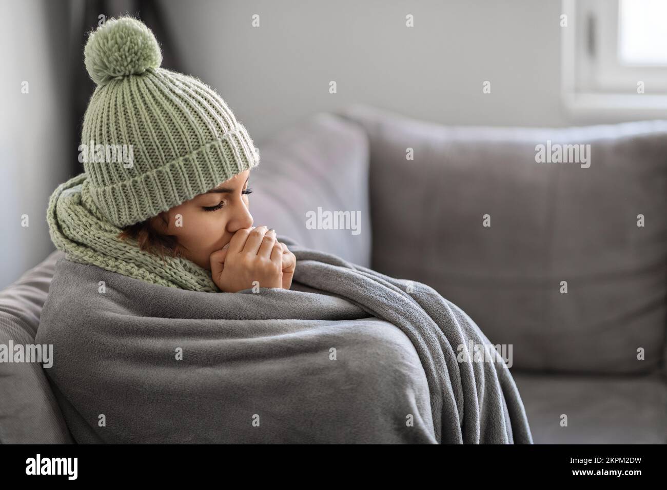 Erfrierende Frau, Die Sich Die Hände Mit Atem Erwärmt, Während Sie Zu Hause Auf Der Couch Sitzt Stockfoto