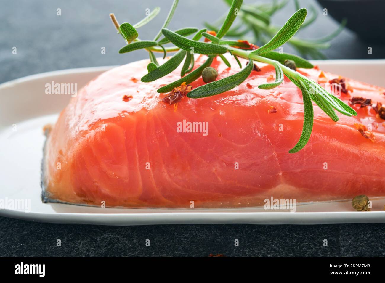 Lachsfischstück. Frisches rohes Lachsfischstück auf Marmorbrett mit Kräutern und Zitrone auf schwarzem Hintergrund. Meeresfrüchte- oder Menükonzept. Draufsicht. Stockfoto