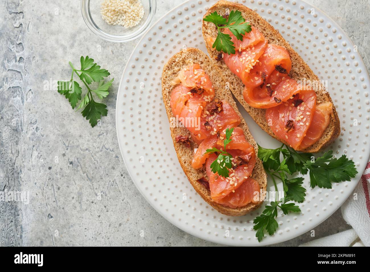 Sandwiches mit gesalzenem Lachs. Offene Sandwiches aus Getreide- oder Vollkorn-Roggenbrot mit gesalzenem Lachs, Sesam und getrockneten Tomaten auf weißem Marmor Stockfoto
