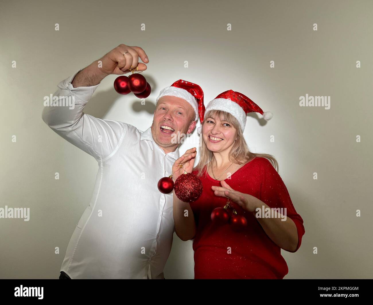 Partyeinladung Neujahr und Weihnachtsmann und -Frau Erwachsene tanzen in den Händen mit Spielzeug, haben Weihnachtshüte auf dem Kopf und rote Bälle Ded Moroz Weihnachtsmann Schneemädchen Stockfoto