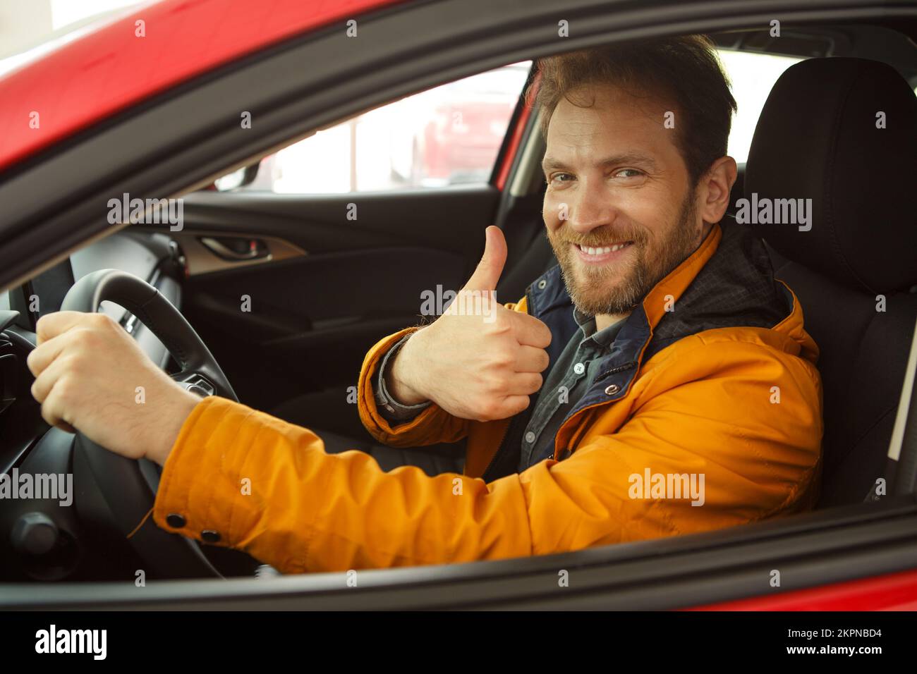 Fröhlicher rothaariger Mann, der im Fahrzeug sitzt, lächelt und super zeigt. Stockfoto