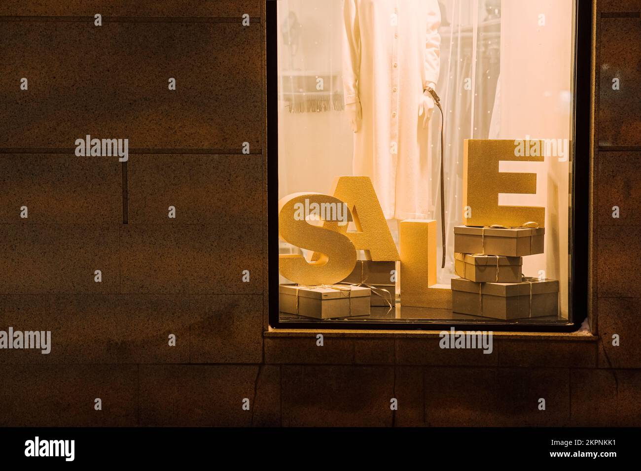 Modekomposition des BRIEFVERKAUFS in der Boutique von der Straßenseite. Schaufenster mit Sale Installation am Abend, goldene Einrichtung, Stockfoto