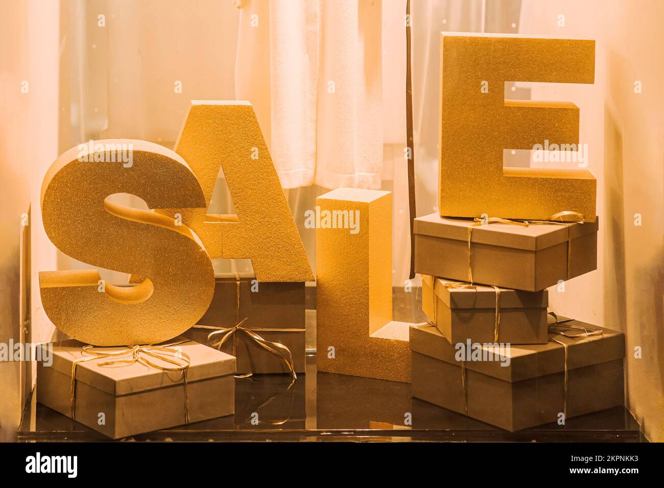 Modekomposition des BRIEFVERKAUFS in der Boutique von der Straßenseite. Schaufenster mit Sale Installation am Abend, goldene Einrichtung, Stockfoto
