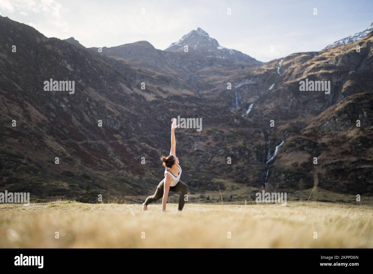 Frau, die Yoga-Dreieck-Pose mit gebeugtem Knie auf einer alpinen Wiese macht, Gastein, Österreich Stockfoto