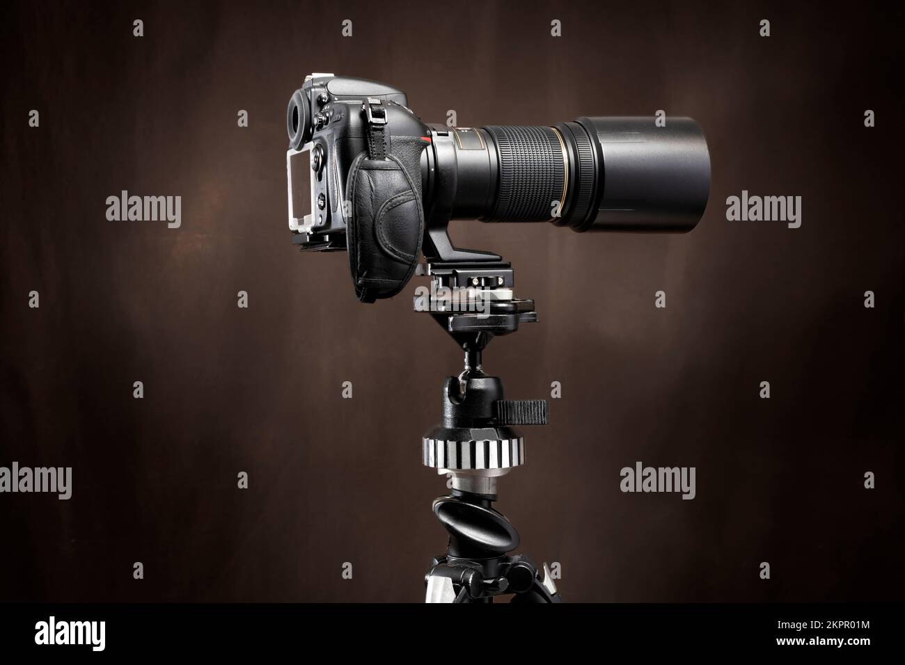 Horizontale Seitenaufnahme einer digitalen Spiegelreflexkamera mit langem Objektiv auf einem Stativ mit braunem Hintergrund und Kopierbereich. Stockfoto