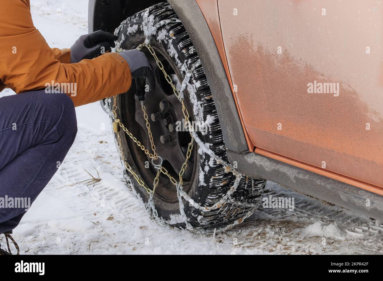 Der Fahrer installiert im Winter Ketten am Rad seines Autos. Fahrzeugausrüstung für Geländeeinsatz und schlechtes Wetter. Stockfoto