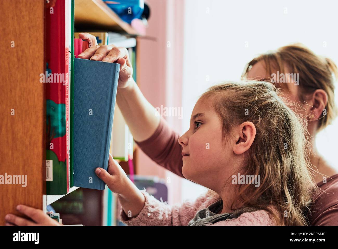 Eine kleine Vorschulkinderin, die ein Buch zum Lesen aussucht. Ein Kind mit seiner Mutter, das