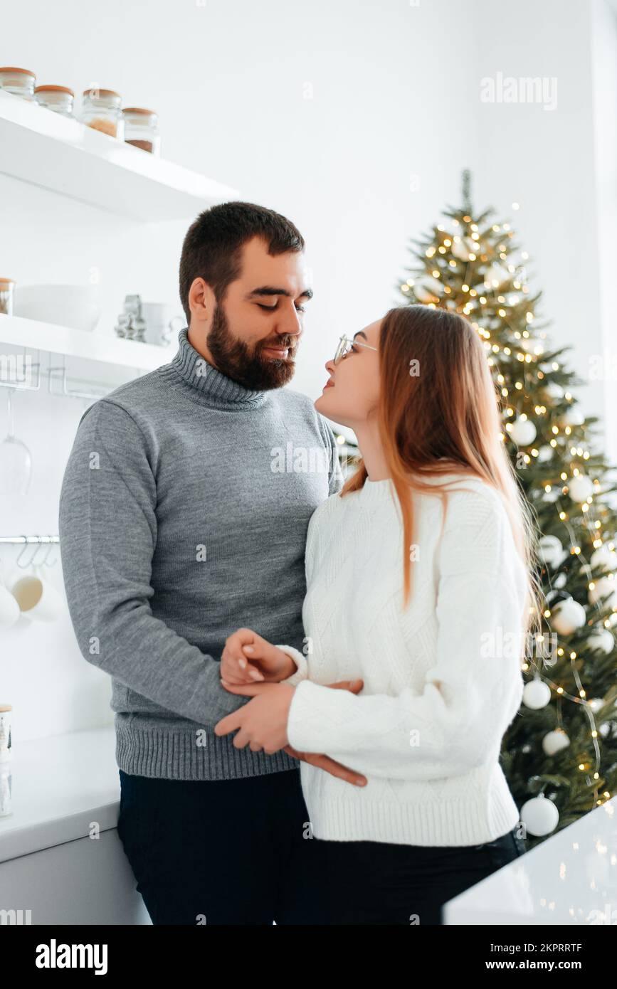 Ein junger Mann und ein junges Mädchen, die sich lieben, umarmen und küssen sich in gemütlichen Pullover neben einem kleinen Weihnachtsbaum Stockfoto