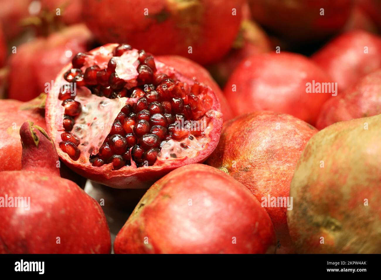 Rote saftige Granatäpfel mit Samen aus nächster Nähe. Ganze und halbe Granatäpfel auf dem Markt, natürlicher Hintergrund Stockfoto